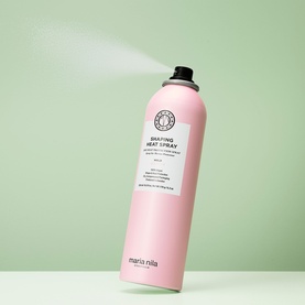 Maria Nila Shaping Heat Spray in pink aerosol can, shown actively dispensing mist against a soft green background