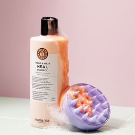Maria Nila Head & Hair Heal Shampoo bottle in beige with black cap, styled alongside a purple scalp massage brush