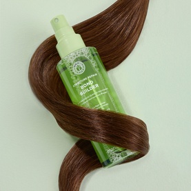 Maria Nila Bond Builder spray bottle in green packaging, nestled within a curl of shiny chestnut hair on a green background
