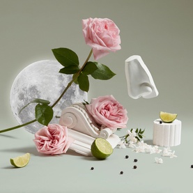 Penhaligon Bath & Body product styled with pink roses, lime slices, marble column, and scattered peppercorns on a sage green background