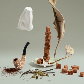 Penhaligon EDP fragrance lifestyle shot with pipe, spices, sugar cubes, vanilla, butterfly and sculptural elements on sage green background