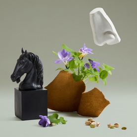Penhaligon's EDP fragrance lifestyle shot with black horse sculpture, terracotta vase with purple flowers, white bottle, and scattered pistachios