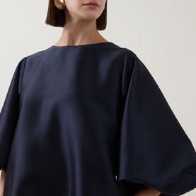 Model wearing Roisin Linnane Olivia Mini Dress in navy, featuring wide sleeves and a boat neckline, styled with gold earrings.