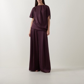 Model wearing Roisin Linnane wine draped top with flutter sleeves, styled with matching wide-leg trousers.
