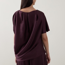 Model wearing Roisin Linnane Wine Top, rear view showing draped back detail and flutter sleeves, styled with matching wide-leg trousers.