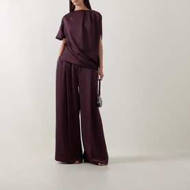 Model wearing Roisin Linnane wine draped short-sleeve top, styled with wide-leg trousers and small black bag.