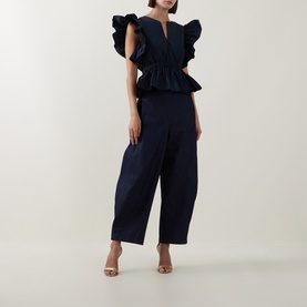 Model wearing Roisin Linnane navy ruffle-sleeve peplum top, styled with matching wide-leg trousers and gold heeled sandals.