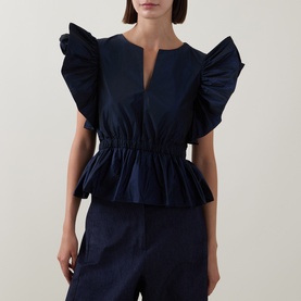 Model wearing Roisin Linnane Navy Top with exaggerated ruffle sleeves, deep V-neckline, cinched waist and peplum hem, styled with navy trousers.