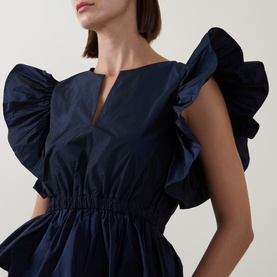 Model wearing Roisin Linnane navy top with dramatic ruffle sleeves, V-neckline, and elasticated waist detail.