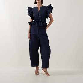 Model wearing Roisin Linnane Navy Top with dramatic ruffle sleeves and peplum waist, styled with wide-leg trousers and gold heeled mules.