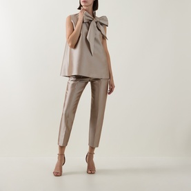 Model wearing Roisin Linnane Mya Bow-Detail Top in gold with matching gold tapered trousers and nude heeled sandals.