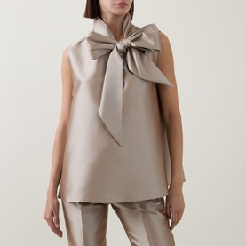 Model wearing Roisin Linnane Mya Bow-Detail Top in gold, sleeveless with oversized bow neckline, styled with matching wide-leg trousers.