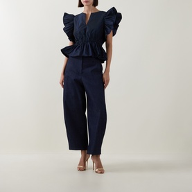 Model wearing Roisin Linnane navy cotton trousers, styled with matching navy ruffle top and gold heeled sandals.