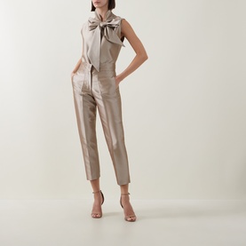 Model wearing Roisin Linnane Twig Cropped Slim-Leg Trousers in gold satin finish, styled with matching sleeveless bow-neck top and nude heeled
