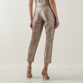 Model wearing Roisin Linnane Twig Cropped Slim-Leg Trousers in gold satin finish, styled with strappy heeled sandals, rear view