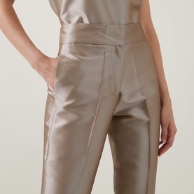 Model wearing Roisin Linnane Twig Cropped Slim-Leg Trousers in gold satin finish, mid-rise with pressed creases and side pockets, styled with
