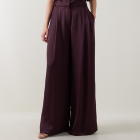 Model wearing Roisin Linnane wine wide-leg trousers with pleated front detail in satin-finish viscose blend fabric.