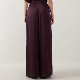 Model wearing Roisin Linnane wine wide-leg satin trousers, rear view, with high-waisted silhouette and fluid drape.