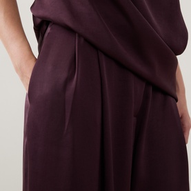 Model wearing Roisin Linnane wine trousers, close-up showing pleated waistband detail and side pocket in fluid drape fabric.