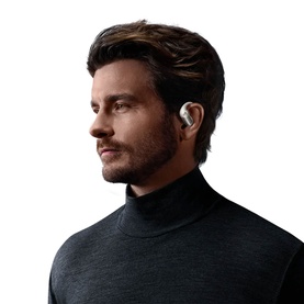 Model wearing open-ear wireless earbuds, shown in profile view, styled with a dark grey roll-neck jumper