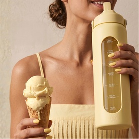 Model with The Head Plan Daily Drench Water Bottle in yellow glass with measurement markings and straw lid, styled with ice cream cone