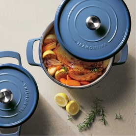 Tramontina blue cast iron casserole dish with lid, filled with roast meat and vegetables, styled with lemon and rosemary on stone surface