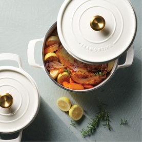 Tramontina latte casserole dish with gold knob lid, filled with roasted meat, carrots and lemon, styled with rosemary on grey surface