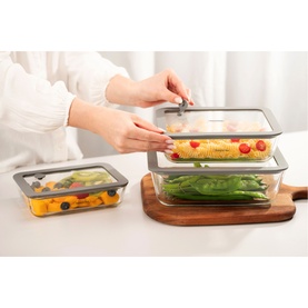 Tramontina clear glass food storage containers with grey lids, shown stacked with fresh vegetables, on wooden board and kitchen surface