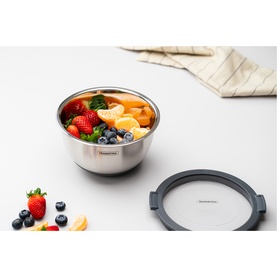 Tramontina stainless steel container filled with fresh fruit, shown with grey silicone lid beside scattered berries and biscuits on white surface.