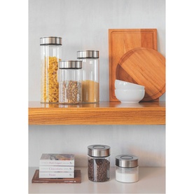 Tramontina clear glass storage containers with stainless steel lids, displayed on wooden shelves with dry foods, alongside a cutting board and bowl.