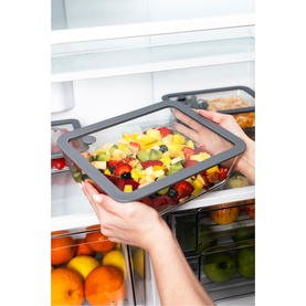 Tramontina clear food storage container with dark grey lid held over open fridge, filled with fresh mixed fruit salad