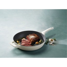 Tramontina latte skillet with cooked steak and vegetables, shown on a teal surface with garlic and herbs