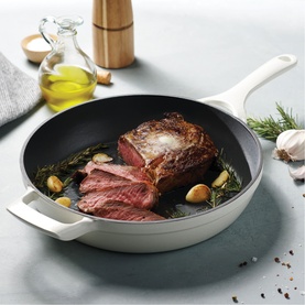 Tramontina latte skillet with seared sliced beef, garlic and herbs, styled with olive oil and pepper grinder on grey surface