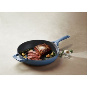Tramontina blue cast iron skillet with seared meat, herbs, and garlic, shown from above on a neutral surface