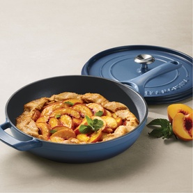 Tramontina blue cast iron saut&eacute; pan filled with peach and chicken dish, lid resting beside, styled with fresh peaches on grey surface