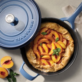 Tramontina blue cast iron saute pan with lid, shown with a peach galette, styled alongside fresh peaches and mint leaves.