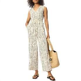 Model wearing Whistles cream sleeveless jumpsuit with black print, belted waist and wide-leg cut, styled with straw tote bag and flat sandals