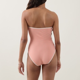 Model wearing Eres pink ribbed strapless one-piece swimsuit with white trim detail, shot from behind.