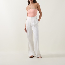 Model wearing Eres pink strapless bandeau swimsuit, styled with white wide-leg trousers and strappy flat sandals