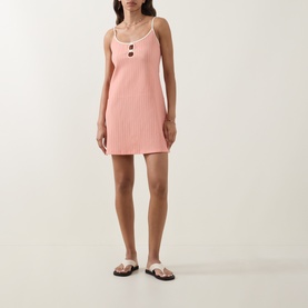 Model wearing Eres pink ribbed knit mini dress with scoop neck and button detail, styled with white strappy flat sandals