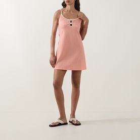 Model wearing Eres pink ribbed mini cover-up dress with spaghetti straps and button detail, styled with white flat sandals