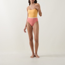 Model wearing Eres pink and yellow colour-block swimsuit with square neckline and high-cut briefs, styled with pearl necklace