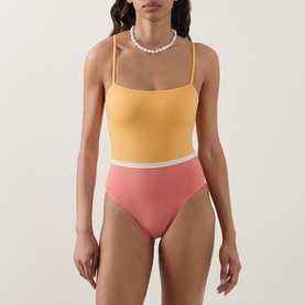 Model wearing Eres pink and yellow colour-block swimsuit with square neckline and high-cut bikini briefs, styled with pearl necklace.