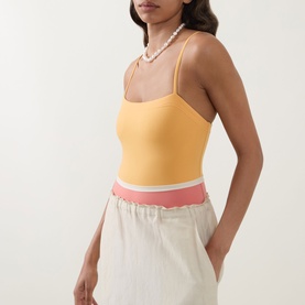 Model wearing Eres pink and yellow swimsuit with spaghetti straps and colour-block waistband, styled with cream wide-leg trousers and pearl necklace
