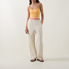 Model wearing Eres swimsuit in pink and yellow, styled with cream wide-leg trousers, pearl necklace and black sandals.