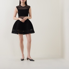 Model wearing Jonathan Simkhai black mini dress with sheer stripe panels, flared skirt, styled with black kitten heel mules