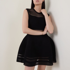 Model wearing Jonathan Simkhai black sleeveless fit-and-flare dress with sheer stripe panels at bodice and hem, gold bracelet