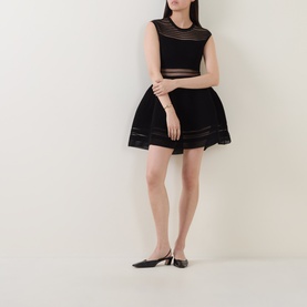 Model wearing Jonathan Simkhai black mini dress with sheer stripe panels, flared skirt, sleeveless design, styled with black pointed kitten heel