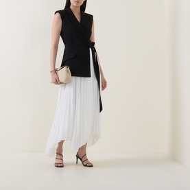 Model wearing Jonathan Simkhai Black Multi Dress with pleated white skirt and tie waist, styled with black heeled sandals and cream clutch bag