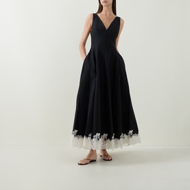 Model wearing Jonathan Simkhai black multi dress with V-neckline, full skirt, and white lace hem trim, styled with tan flat sandals.